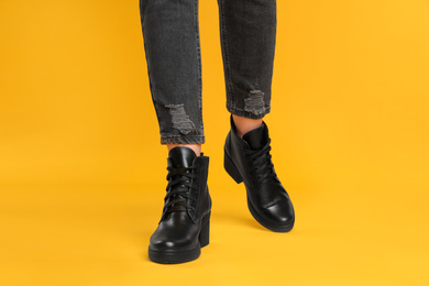 Woman wearing stylish boots on yellow background, closeup