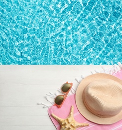 Beach accessories on white wooden deck near swimming pool, flat lay. Space for text 