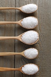 Photo of Organic salt in spoons on wooden table, flat lay