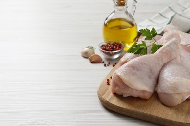 Raw chicken drumsticks and ingredients on white wooden table, space for text