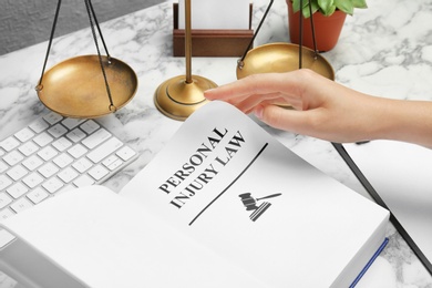 Photo of Woman turning page of book with words PERSONAL INJURY LAW at table, closeup