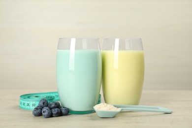 Photo of Tasty shakes with blueberries, measuring tape and powder on wooden table. Weight loss