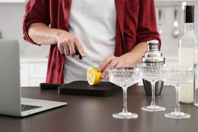 Photo of Man learning to make cocktail with online video on laptop at table in kitchen, closeup. Time for hobby