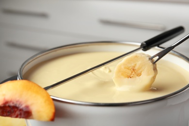 Photo of Dipping fresh banana into pot with chocolate fondue, closeup