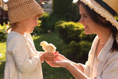 Happy mother and her little daughter with cute chick outdoors