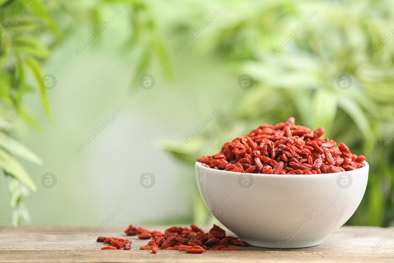 Photo of Bowl of dried goji berries on table against blurred background. Space for text