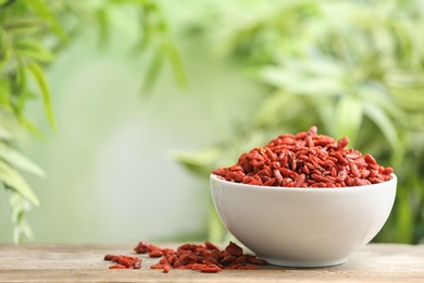 Photo of Bowl of dried goji berries on table against blurred background. Space for text