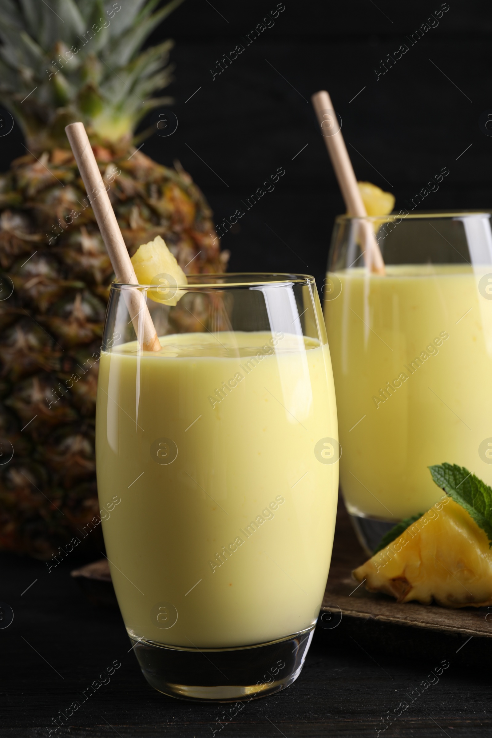 Photo of Tasty pineapple smoothie and fruit on black table