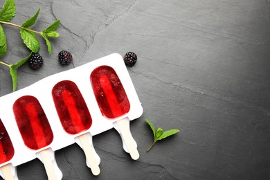 Photo of Tasty berry ice pops in mold and space for text on grey table, flat lay. Fruit popsicle