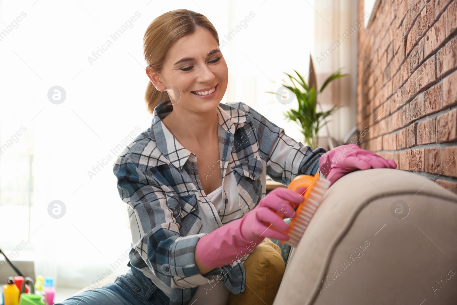 Photo of Portrait of woman cleaning sofa with brush in living room