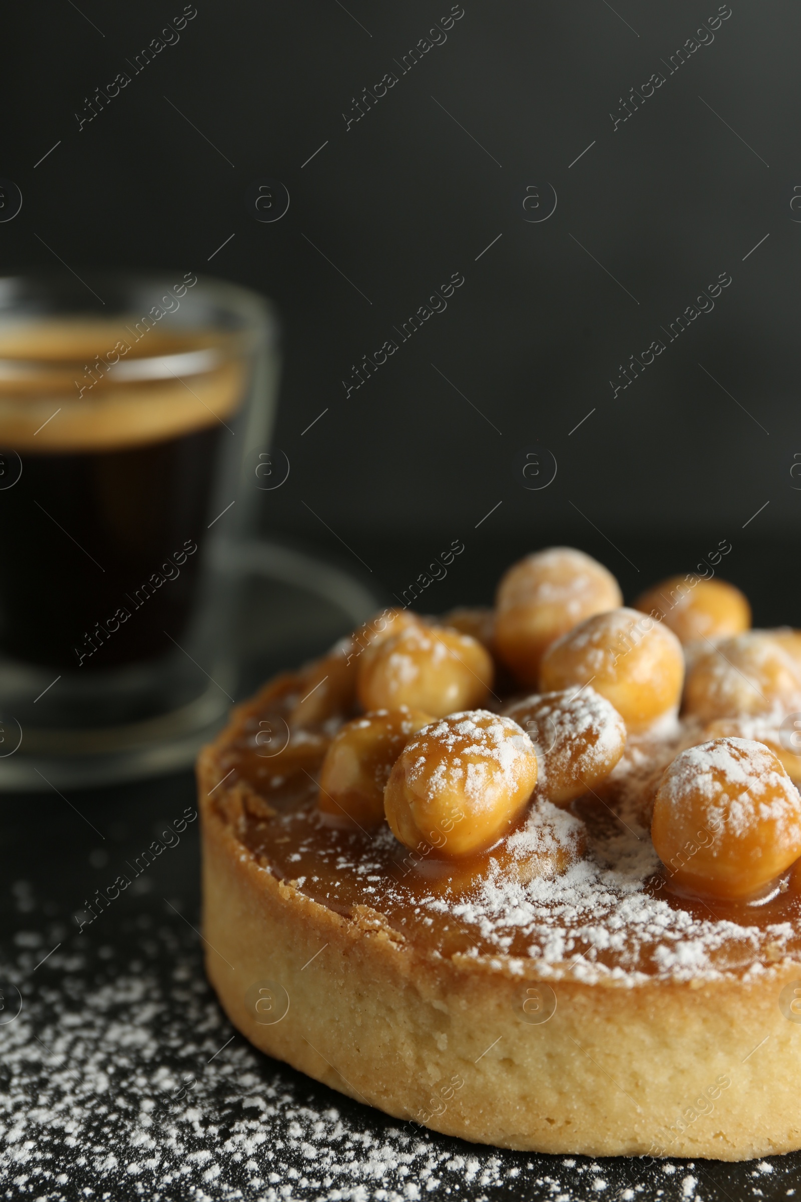 Photo of Delicious tart with hazelnuts, sweet caramel and powdered sugar on black table, closeup