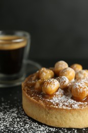 Delicious tart with hazelnuts, sweet caramel and powdered sugar on black table, closeup