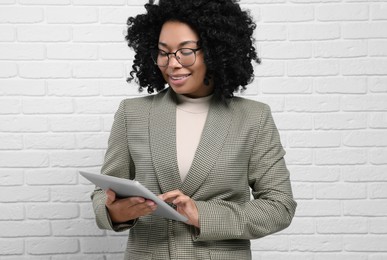 Young businesswoman with tablet near white brick wall