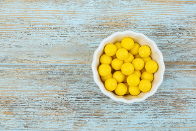 Delicious lemon chewing gums in bowl on light blue wooden background, top view. Space for text