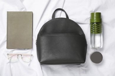 Photo of Stylish urban backpack and different items on white fabric, flat lay