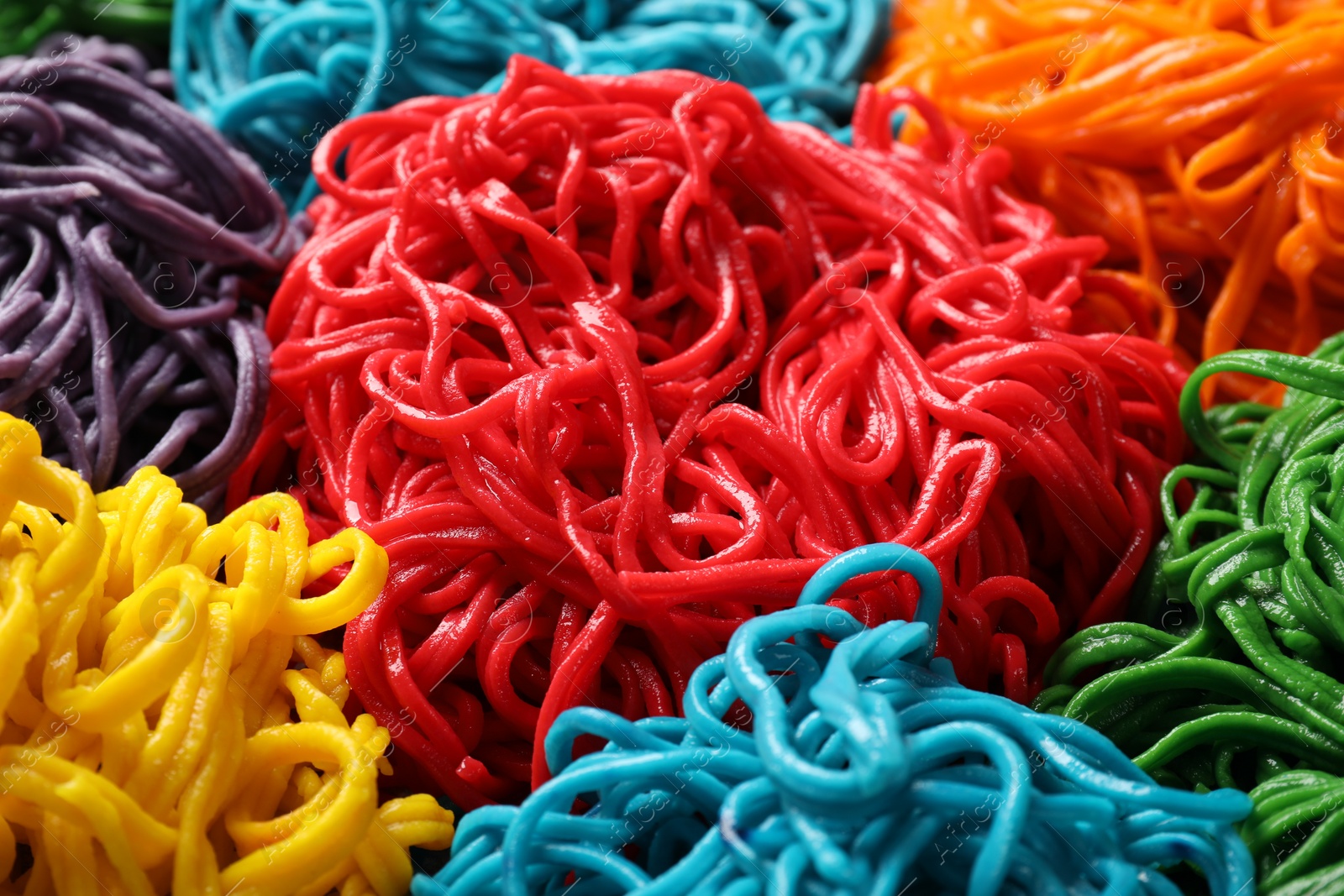 Photo of Rolled spaghetti painted with different food colorings as background, closeup