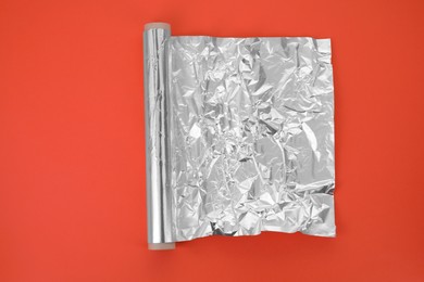 Roll of aluminum foil on orange background, top view