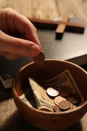 Donate and give concept. Woman putting coin into bowl with money at table, closeup