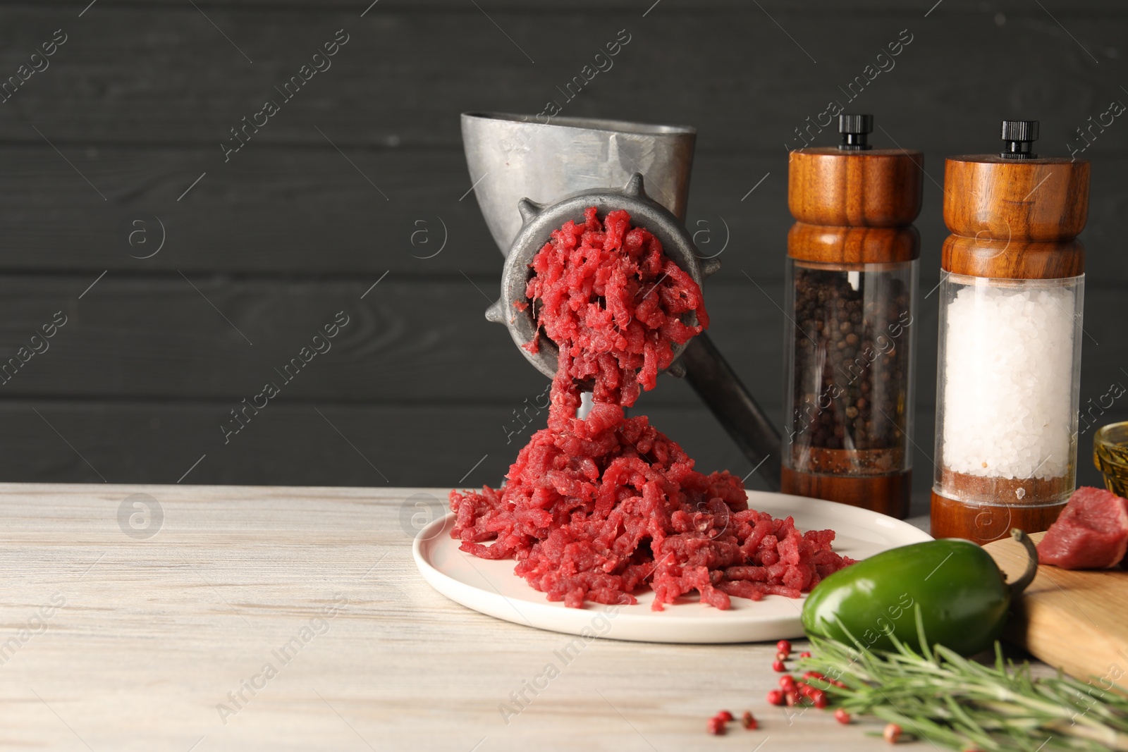 Photo of Metal meat grinder with minced beef, products and spices on light wooden table. Space for text