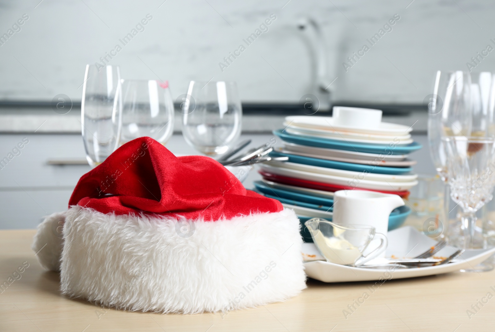 Photo of Santa hat and dirty dishware on wooden table in kitchen after party