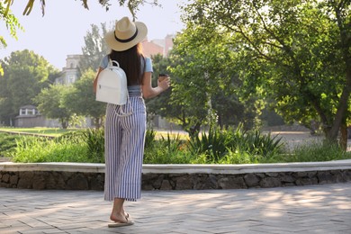 Photo of Young woman with stylish backpack and cup of coffee in city park, back view