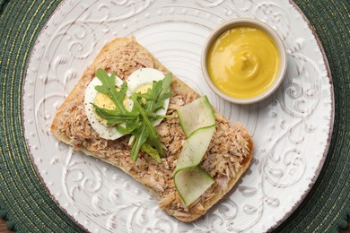 Photo of Delicious sandwich with tuna, boiled egg, vegetables and mustard sauce on green mat, top view