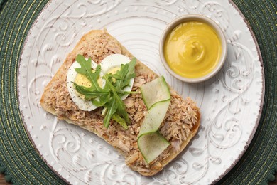 Delicious sandwich with tuna, boiled egg, vegetables and mustard sauce on green mat, top view