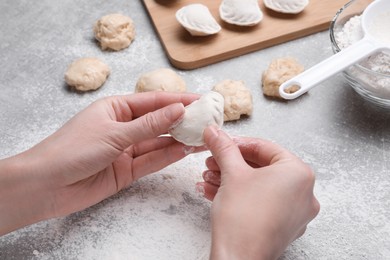 Woman making dumplings (varenyky) at grey table, closeup