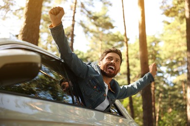 Photo of Enjoying trip. Happy man leaning out of car window, low angle view