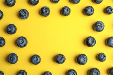 Photo of Frame of ripe blueberries on yellow background, flat lay with space for text