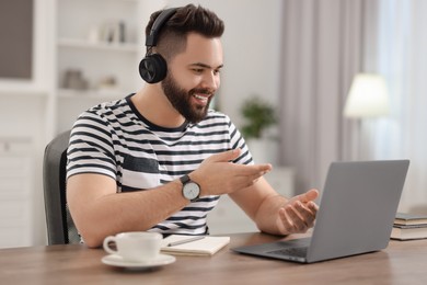 Young man in headphones using video chat during webinar at table in room