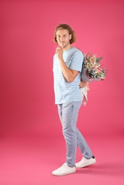 Young handsome man hiding beautiful flower bouquet behind his back on pink background