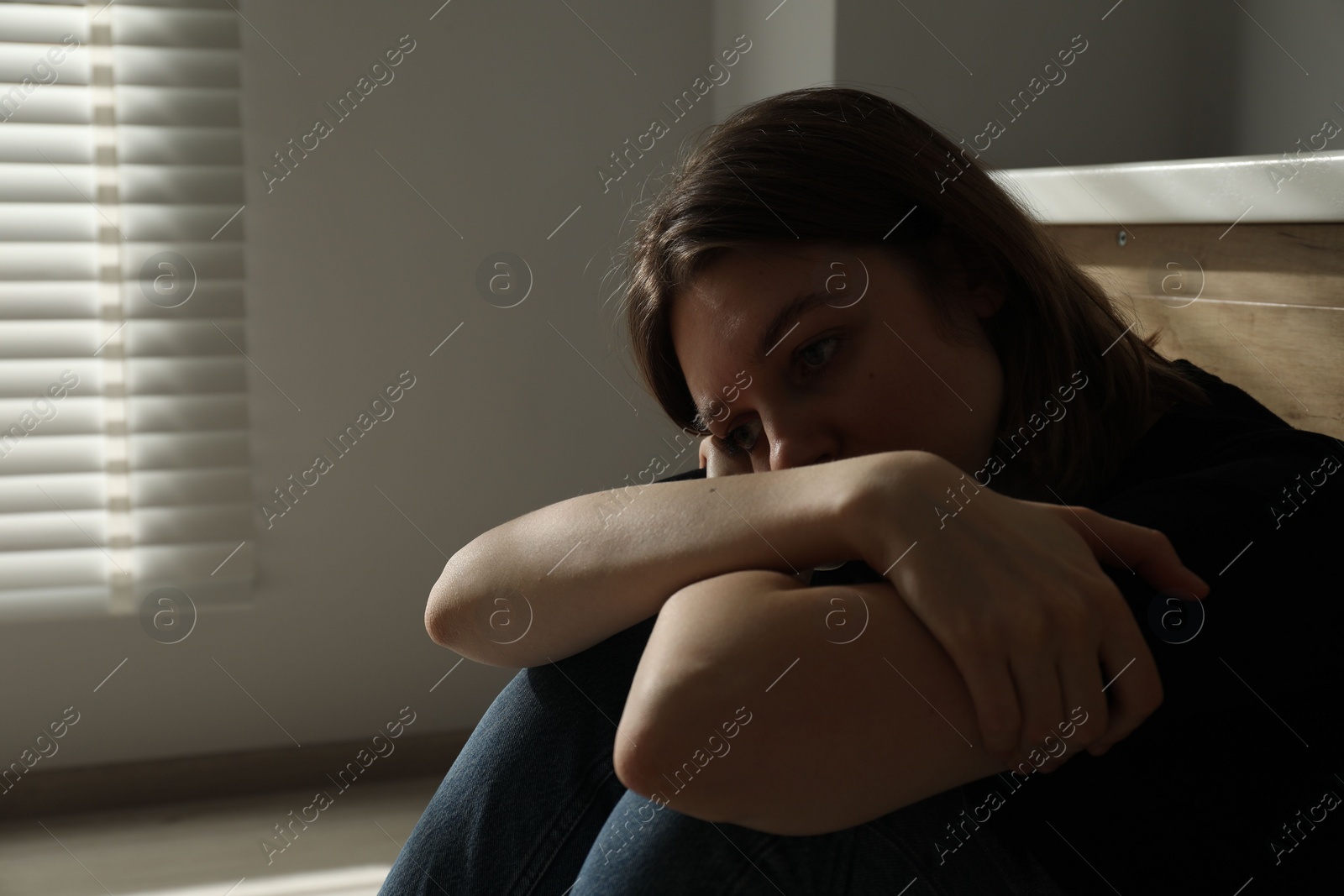 Photo of Sad young woman sitting indoors, space for text