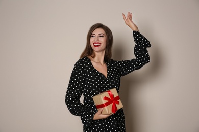 Happy woman with gift box on beige background. Christmas party