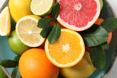 Different cut and whole citrus fruits in bowl, top view