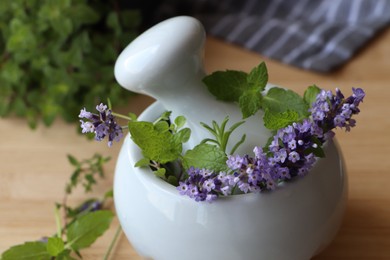 Photo of Mortar with fresh lavender flowers, herbs and pestle on table, closeup