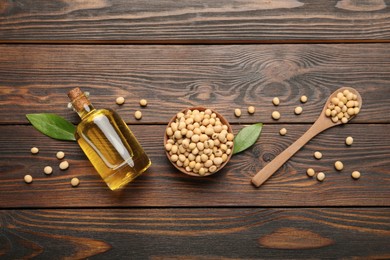 Photo of Bottle of oil and soybeans on wooden table, flat lay