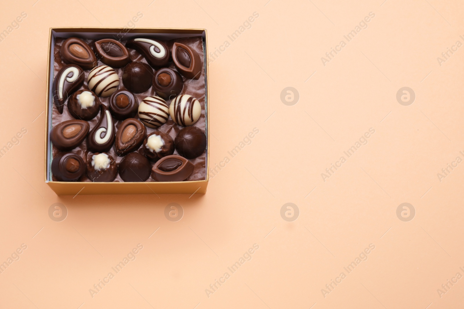 Photo of Box of delicious chocolate candies on beige background, top view. Space for text