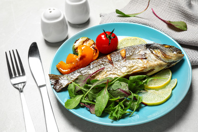 Photo of Delicious roasted fish with lemon and vegetables on grey marble table