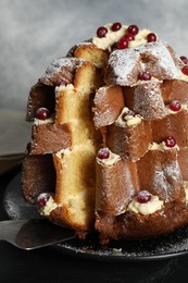 Photo of Taking slice of delicious Pandoro Christmas tree cake with powdered sugar and berries on black table