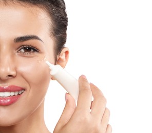 Woman applying cream under eyes on white background, closeup. Skin care