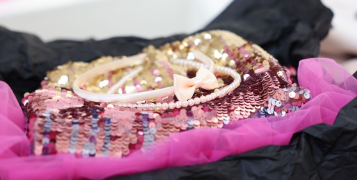 Photo of Headbands and stylish pink carnival costume with sequins in black box, closeup