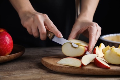 Photo of Woman cutting apple to make traditional English pie at wooden table, closeup