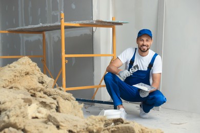 Photo of Professional worker putting plaster on putty knife indoors