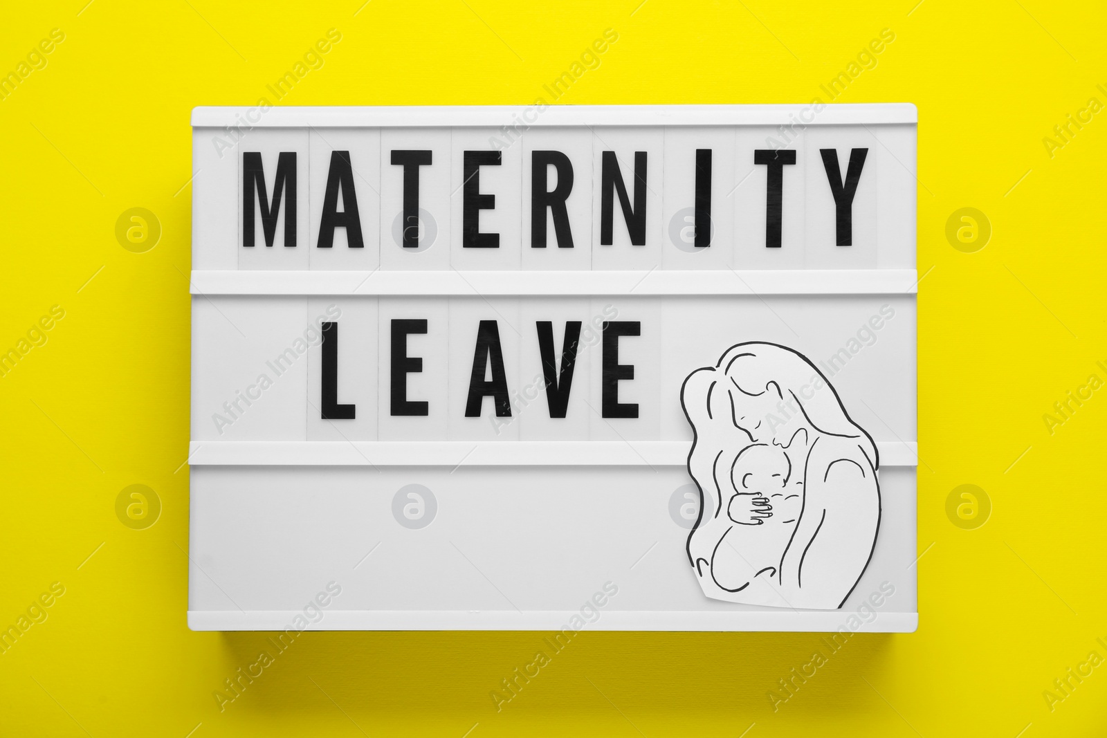 Photo of Maternity leave concept. Lightbox with paper cutout of mother and child on yellow background, top view