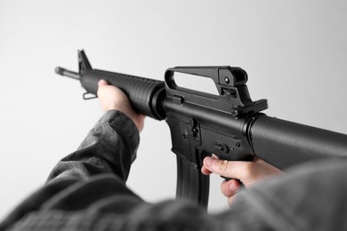 Photo of Assault gun. Man aiming rifle on light background, closeup