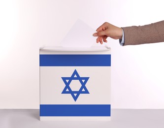 Image of Woman putting her vote into ballot box decorated with flag of Israel against white background, closeup