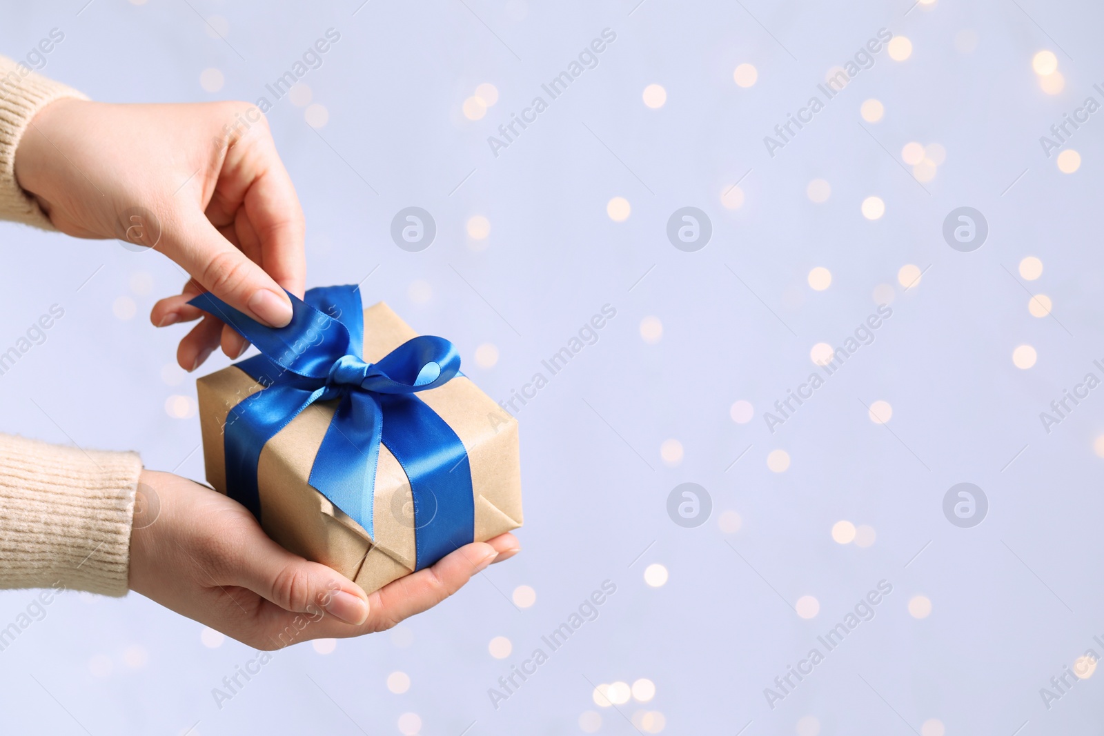 Photo of Woman holding gift box with blue bow against blurred festive lights, closeup and space for text. Bokeh effect