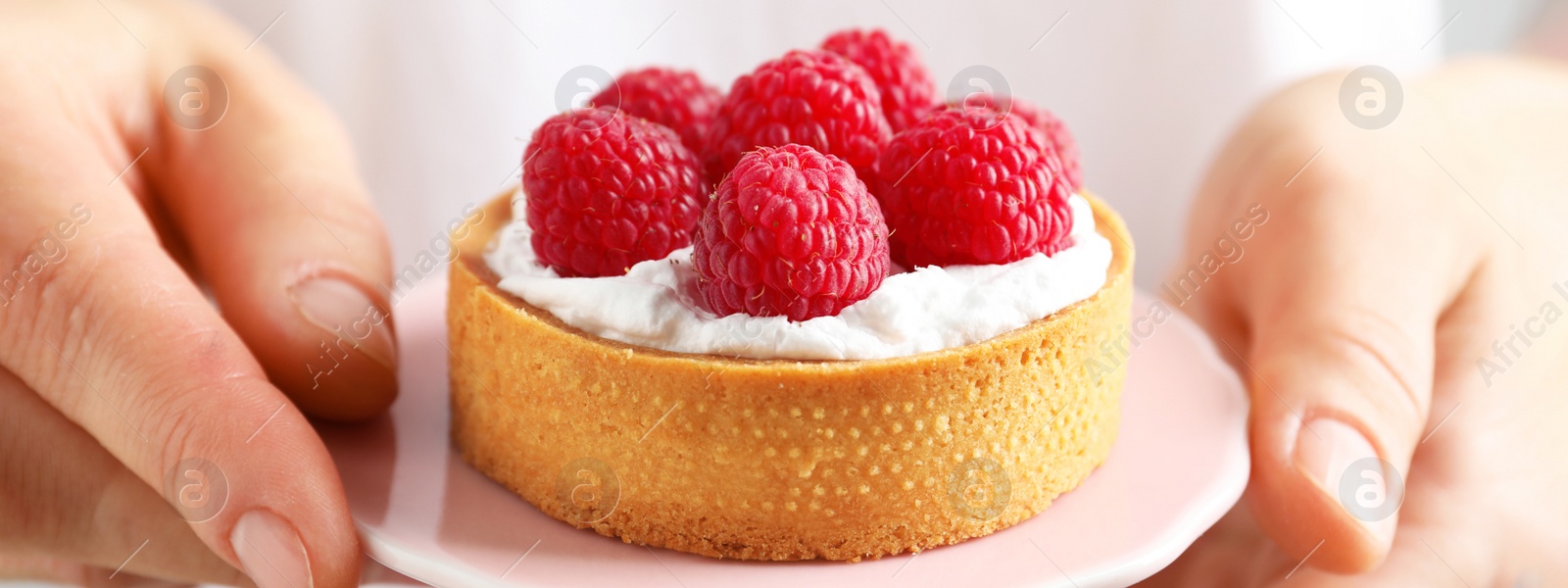 Image of Woman holding cake stand with raspberry tartlet, closeup. Banner design