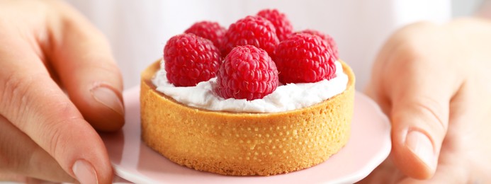 Image of Woman holding cake stand with raspberry tartlet, closeup. Banner design